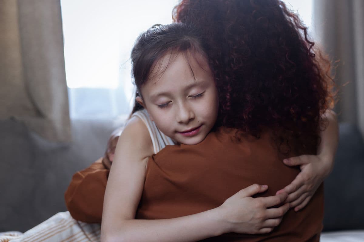 A young girl resting her head on her mother's shoulder in a close hug